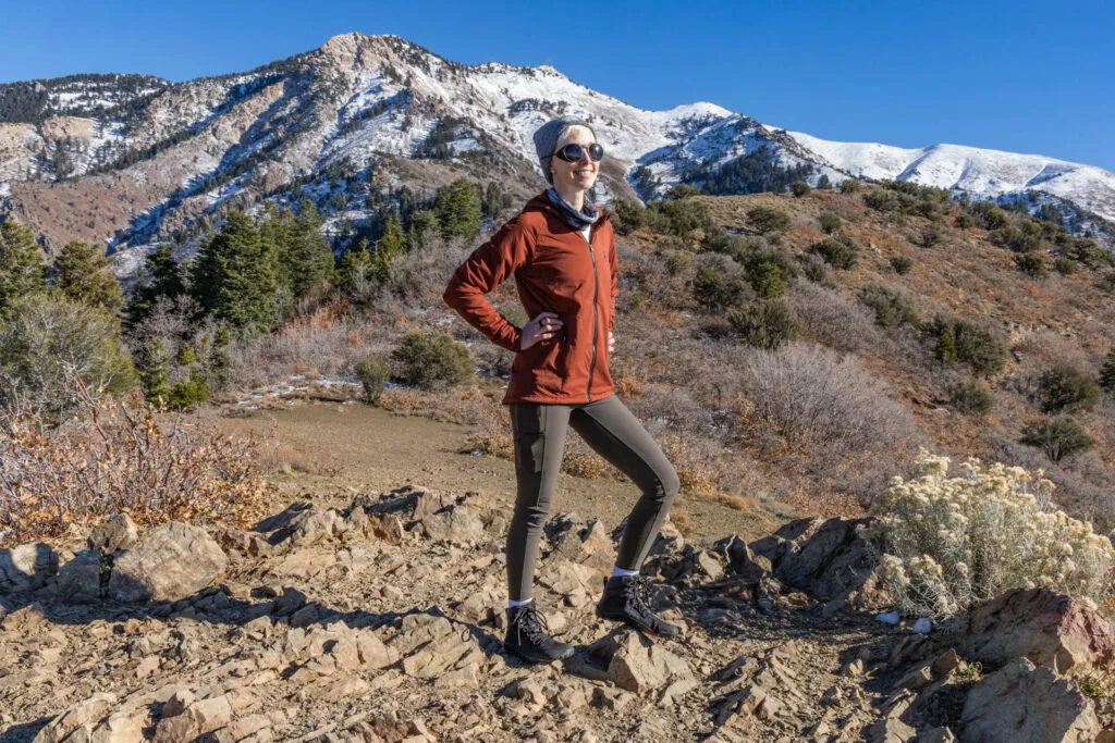 A woman poses on a hiking trail. She is wearing Cotopaxi Verso hiking tights.