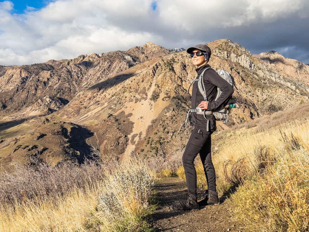 A woman poses on a hiking trail. She is wearing hiking tights.