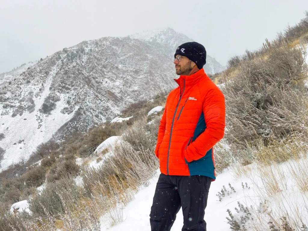 A man stands on a snowy mountain wearing the Jack Wolfskin Routeburn Pro Insulated Jacket.