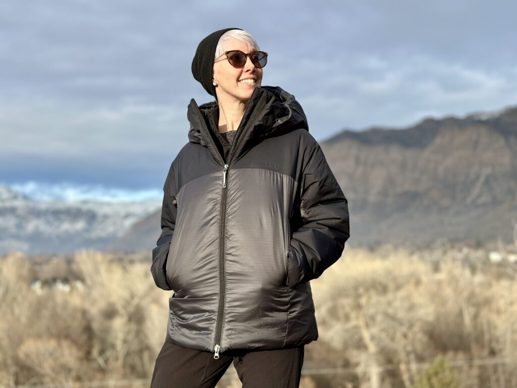 A woman wears the Houdini Double Dunfri in front of mountains.