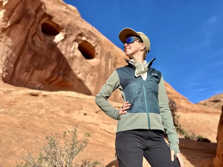 A woman kneels smiling in front of canyon walls wearing a Helly Hansen Versatile Hybrid Fleece Jacket.