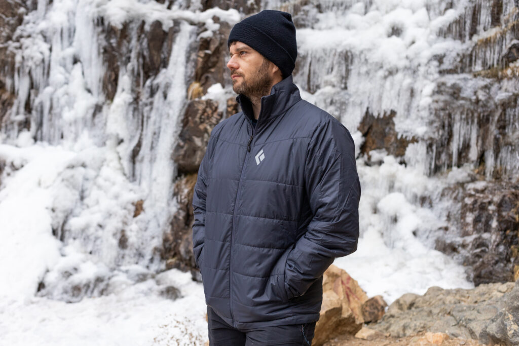 A man stands in front of a frozen waterfall in a Black Diamon Solution Jacket.