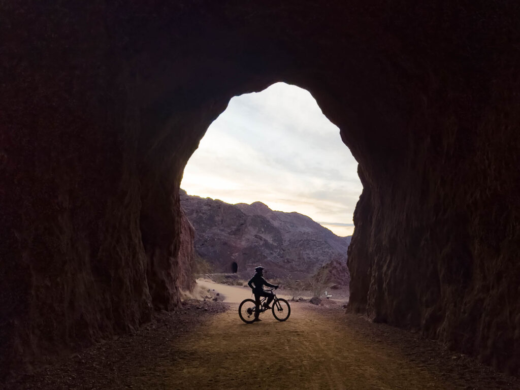 A cyclist pauses at the opening of a dark tunnel to take in the view along Lake Mead Historic Railroad Tunnel Trail.