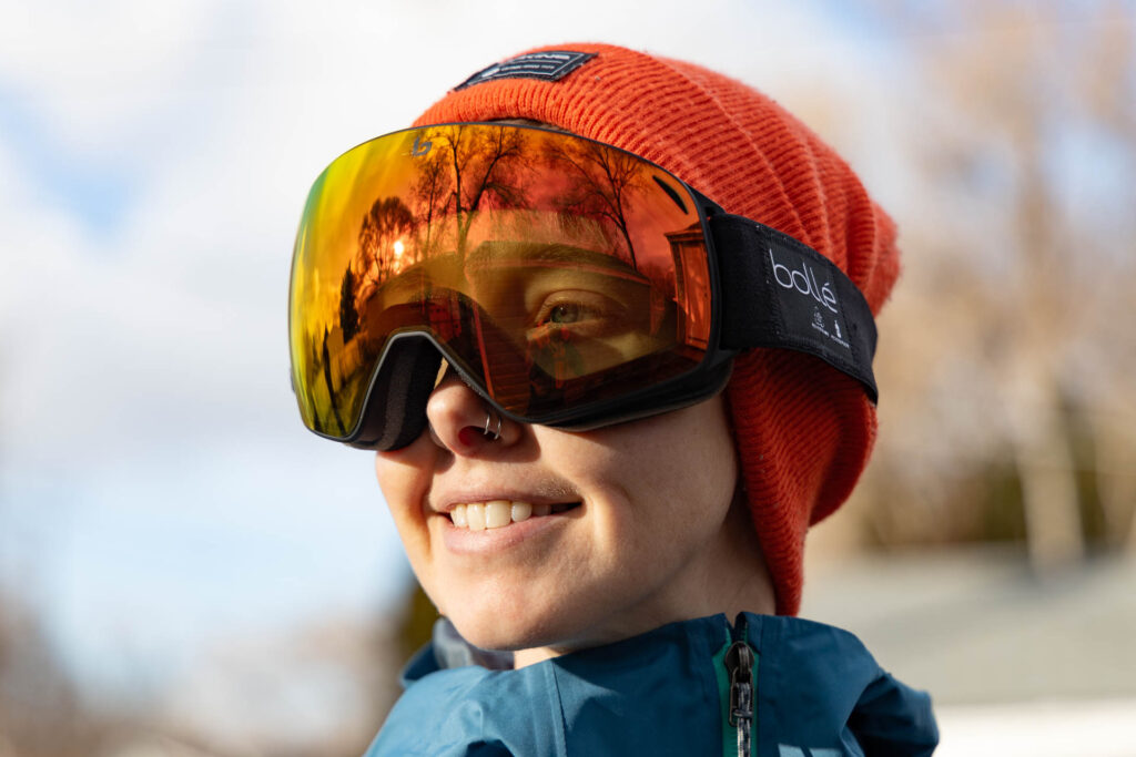 A woman smiles in the Bolle Eco-Torus M ski goggles in Black Matte with Photochromic Sunrise lenses.
