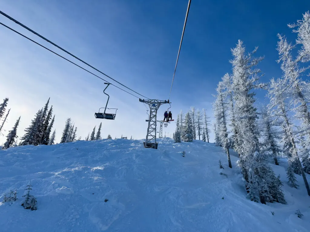 Two people on a chair lift going up the mountain at RED Mountain Resort.