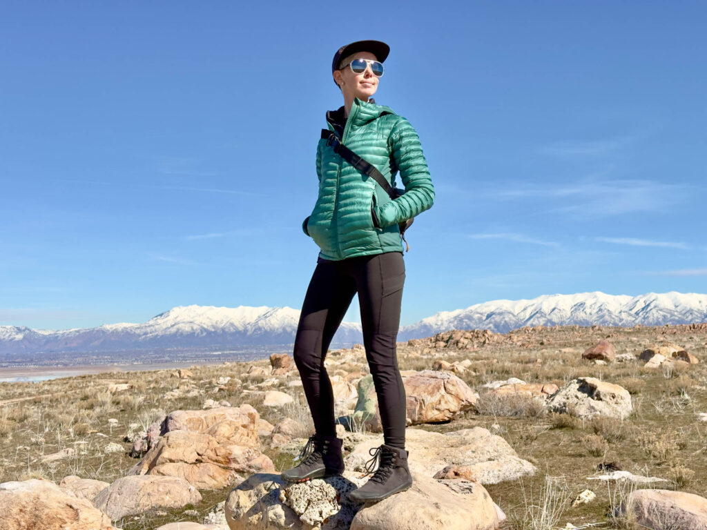 A woman stands on a rock with mountains in the background. She is wearing Mammut Zinal Hybrid Tights.