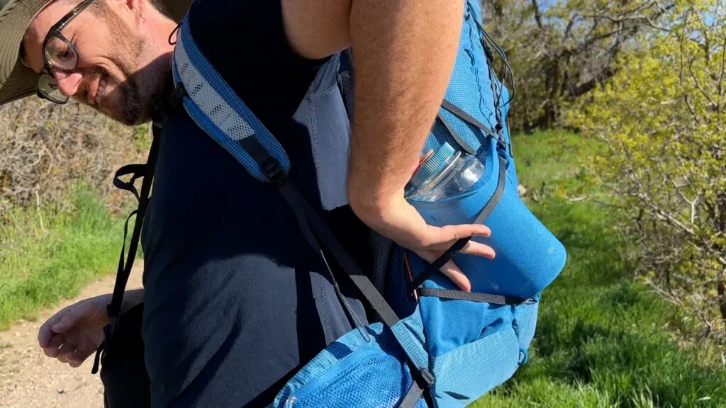 A man reaches around to remove a bottle from the side pockets of The Deuter Aircontact Ultra.