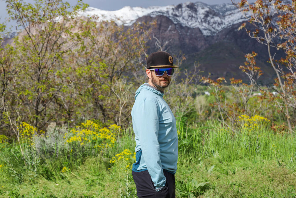 A man stands in front of mountains in the Cotopaxi Sombra Sun Hoodie.