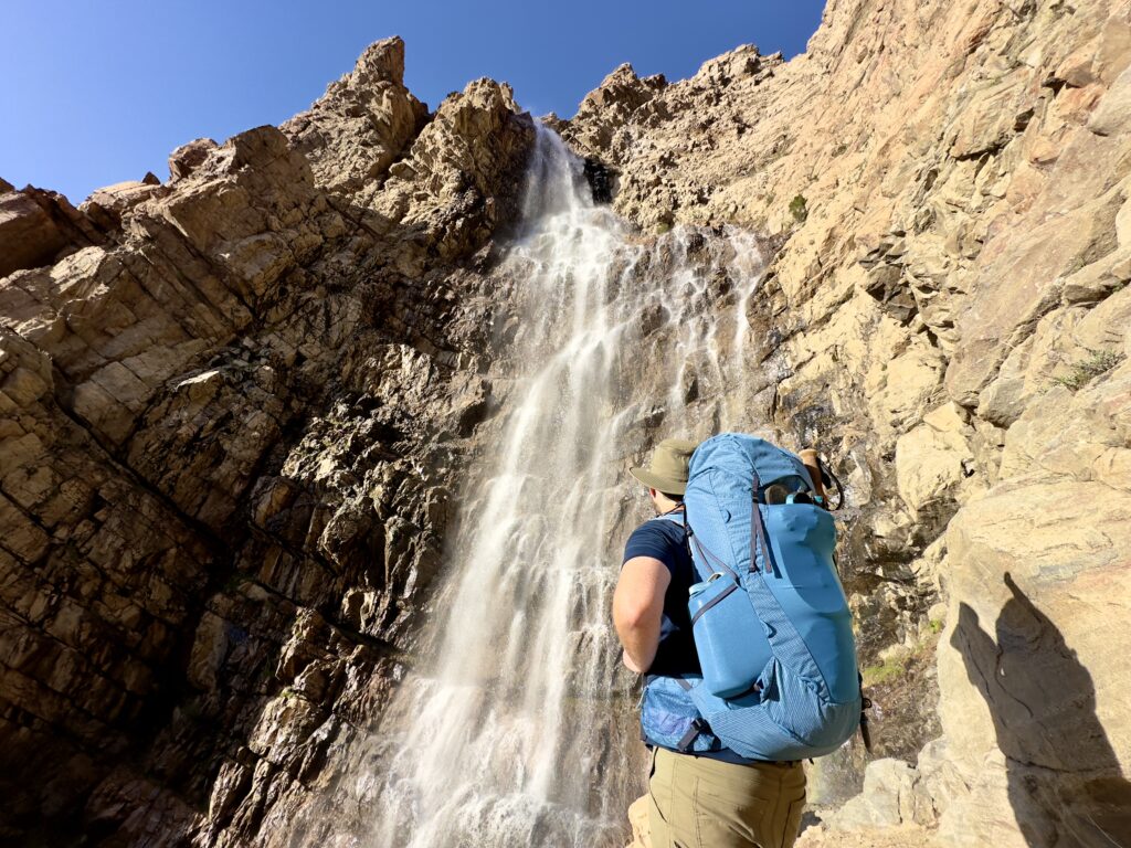A man looks at a waterfall. He is wearing The Deuter Aircontact Ultra.