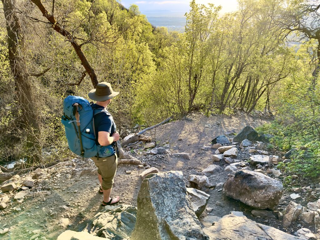 A man on a trail wears a Deuter backpack and sandals.