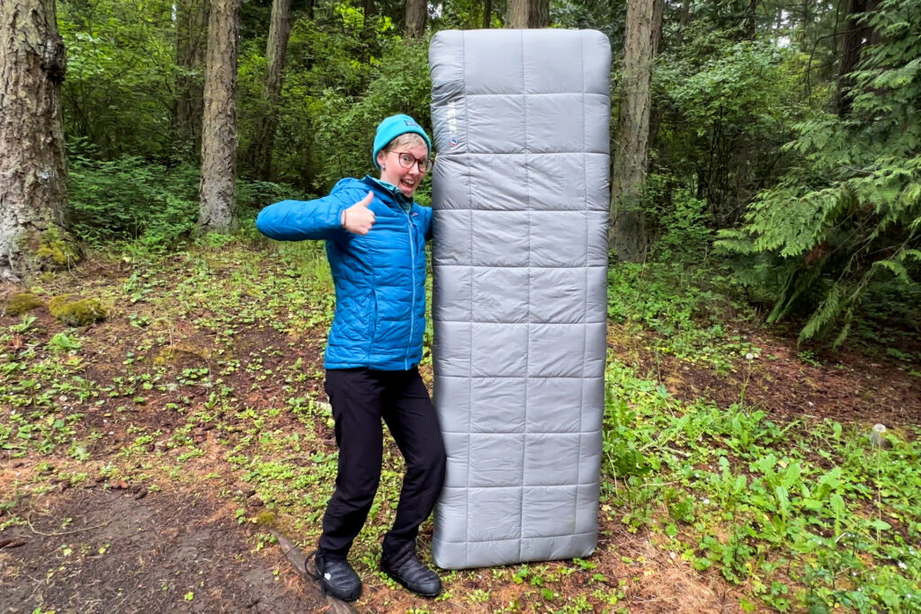 A woman poses with a thumbs up next to a Big Agnes Circle Back Sleeping Pad.
