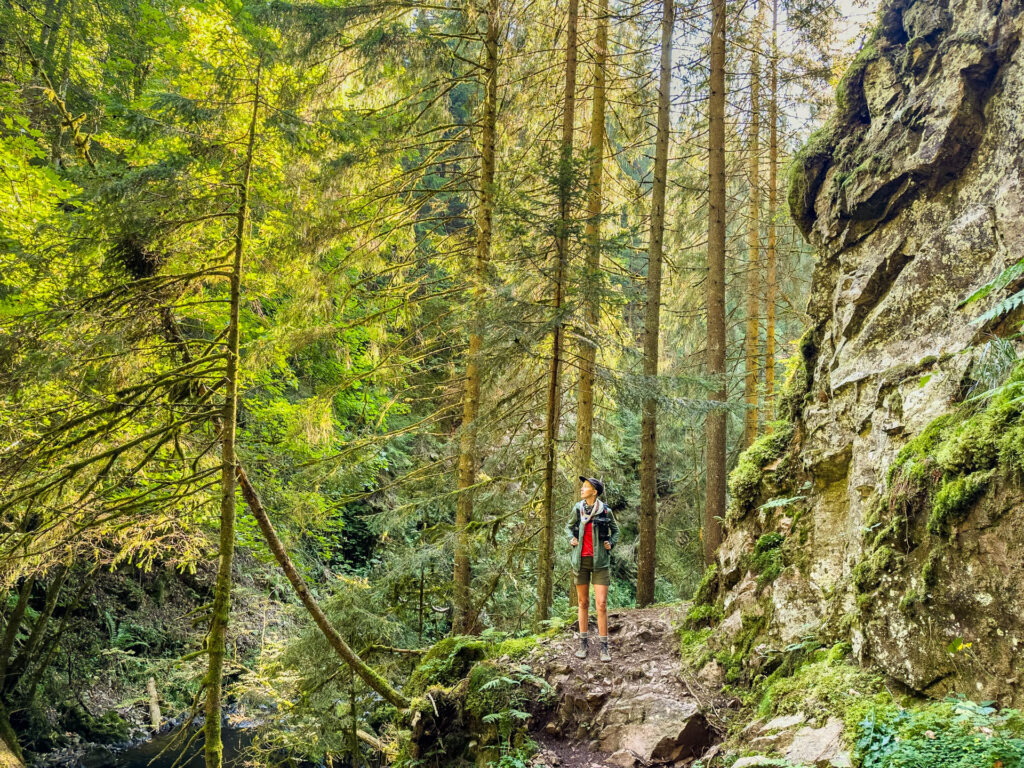 A woman hiking in the woods with a backpack and barefoot shoes.