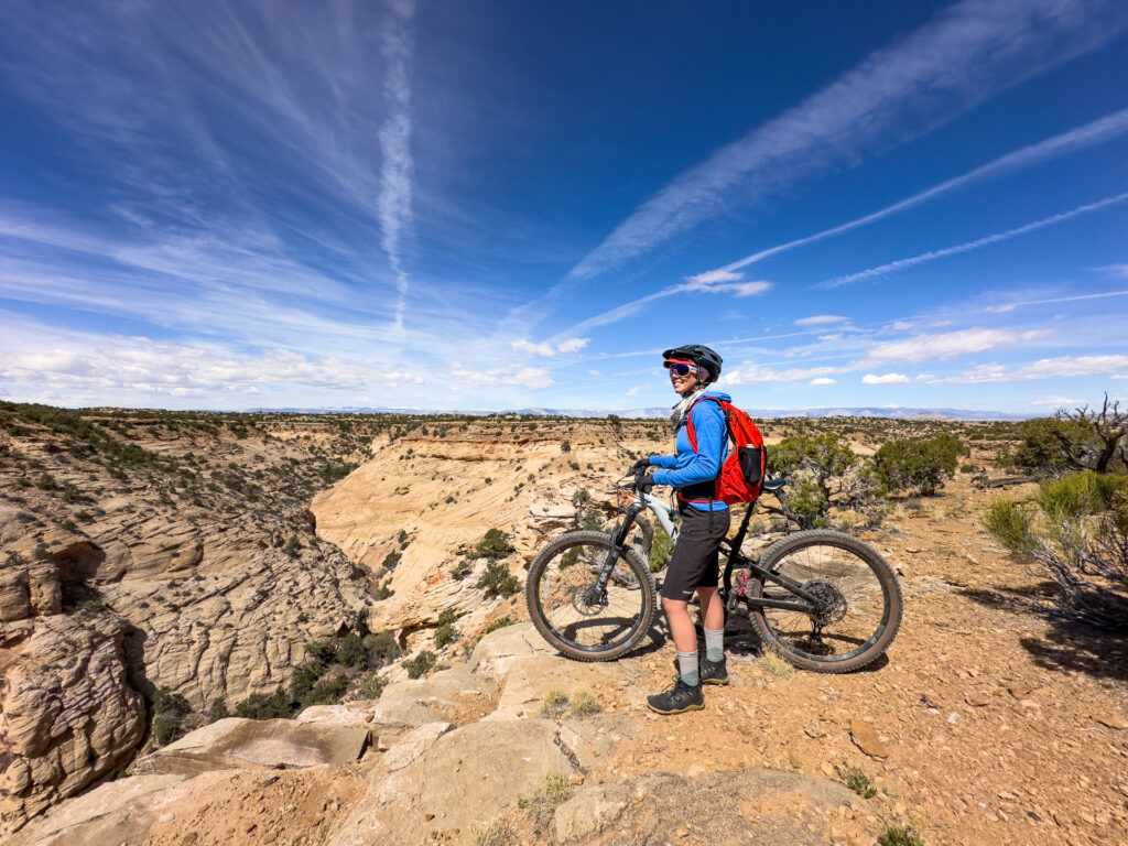 A woman stands smiling with her mountain bike at the edge of a canyon.