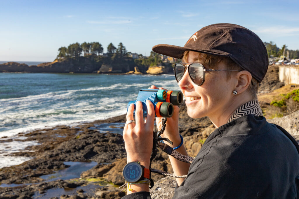 A woman smiles and holds Nocs binoculars while whale watching in Depoe Bay, OR.