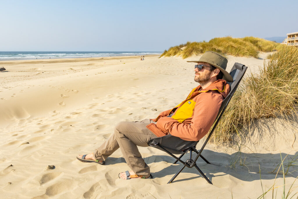 A man sits on the beach in a Helinox Sunset Chair.