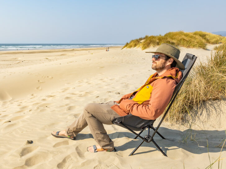 A man sits in a Helios camp chair on the beach.