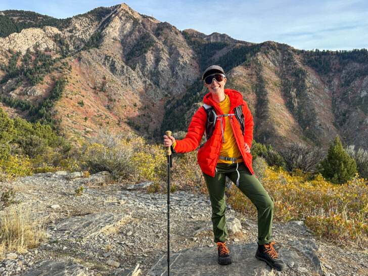 A woman in hiking clothing and Bahé boots smiles in front of a peak.