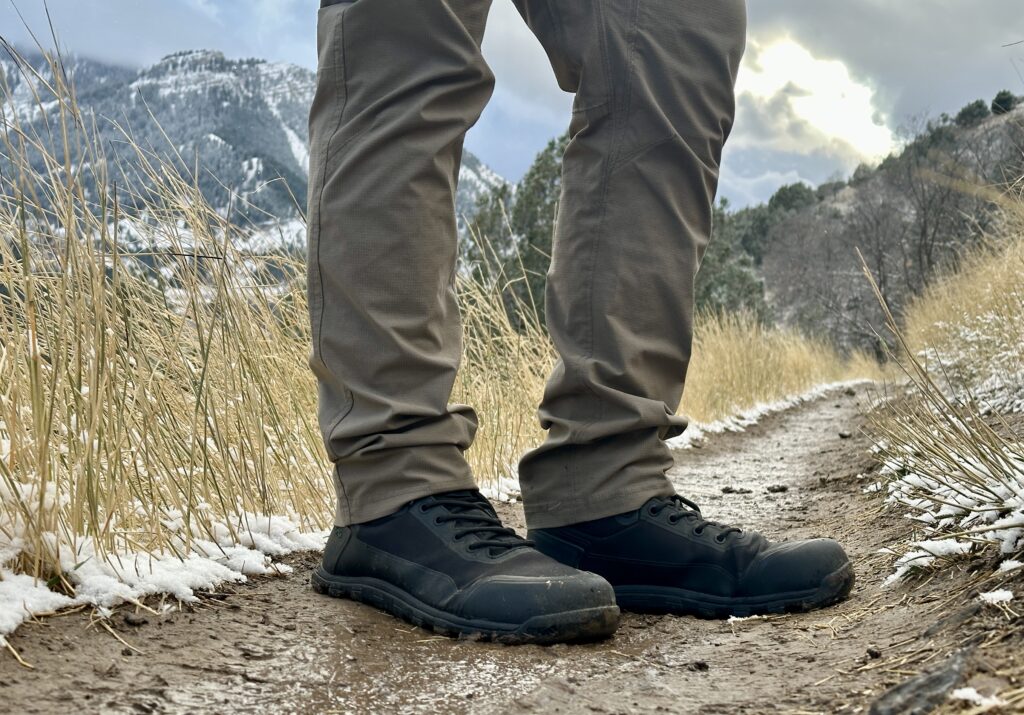 A hiker in Bahé Rediscover boots on a dirt trail with mountain in the background.