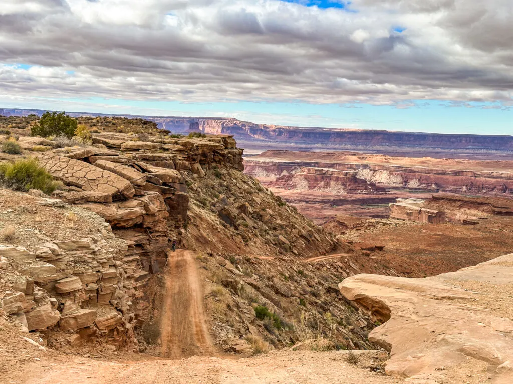 A steep downhill on White Rim Road with canyons and plateaus in the background in Canyonlands National Park.