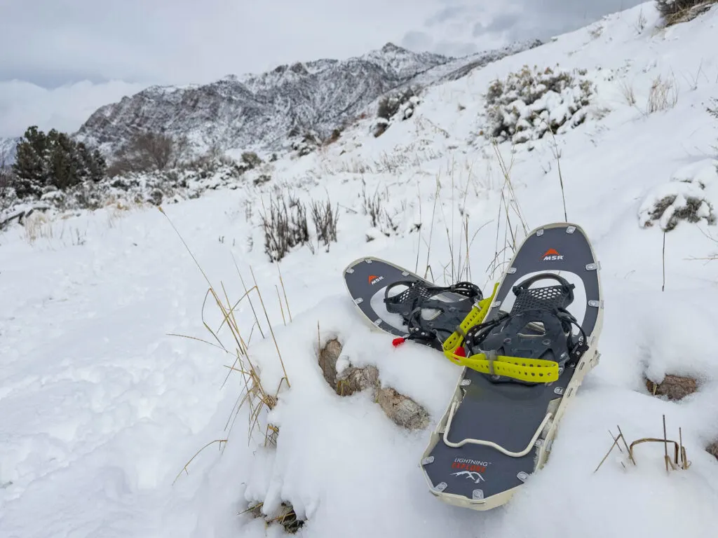 MSR Lightning Explore Snowshoes sitting in the snow in front of a mountain.