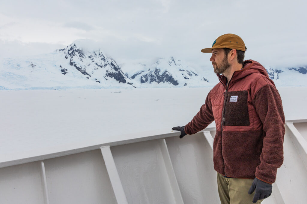 A man stands on the deck of an expedition cruise ship in Antarctica wearing a warm Cotopaxi Trico zip-up.