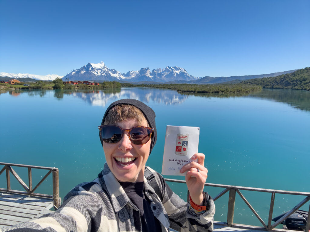 A woman hold up her trekking passport in front of a lake and Torres del Paine after Fjällräven Classic Chile.