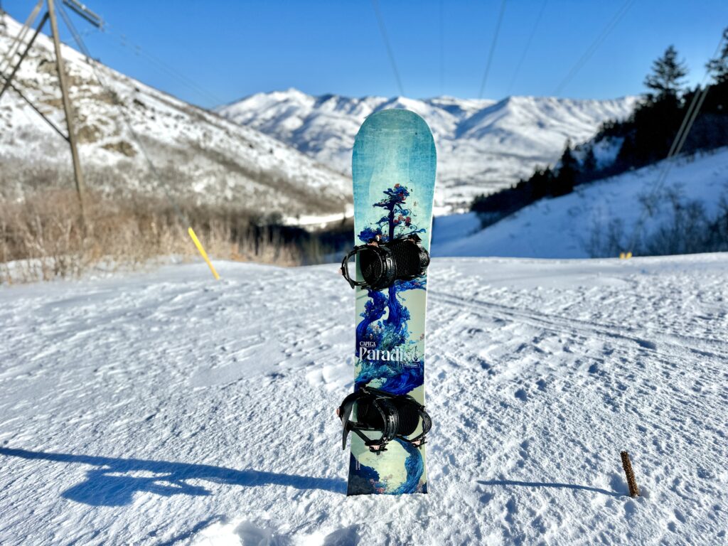 A Capita Paradise snowboard stands up in the snow.