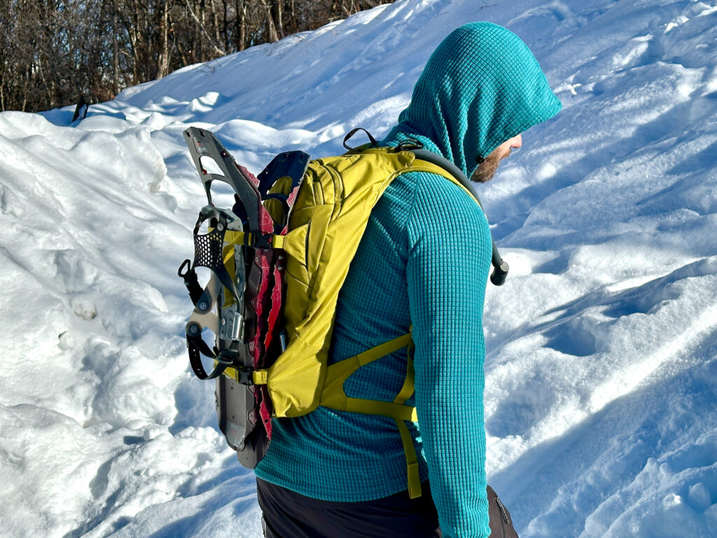 A man wears an Osprey Glade 12 backpack with snowshoes on the back.