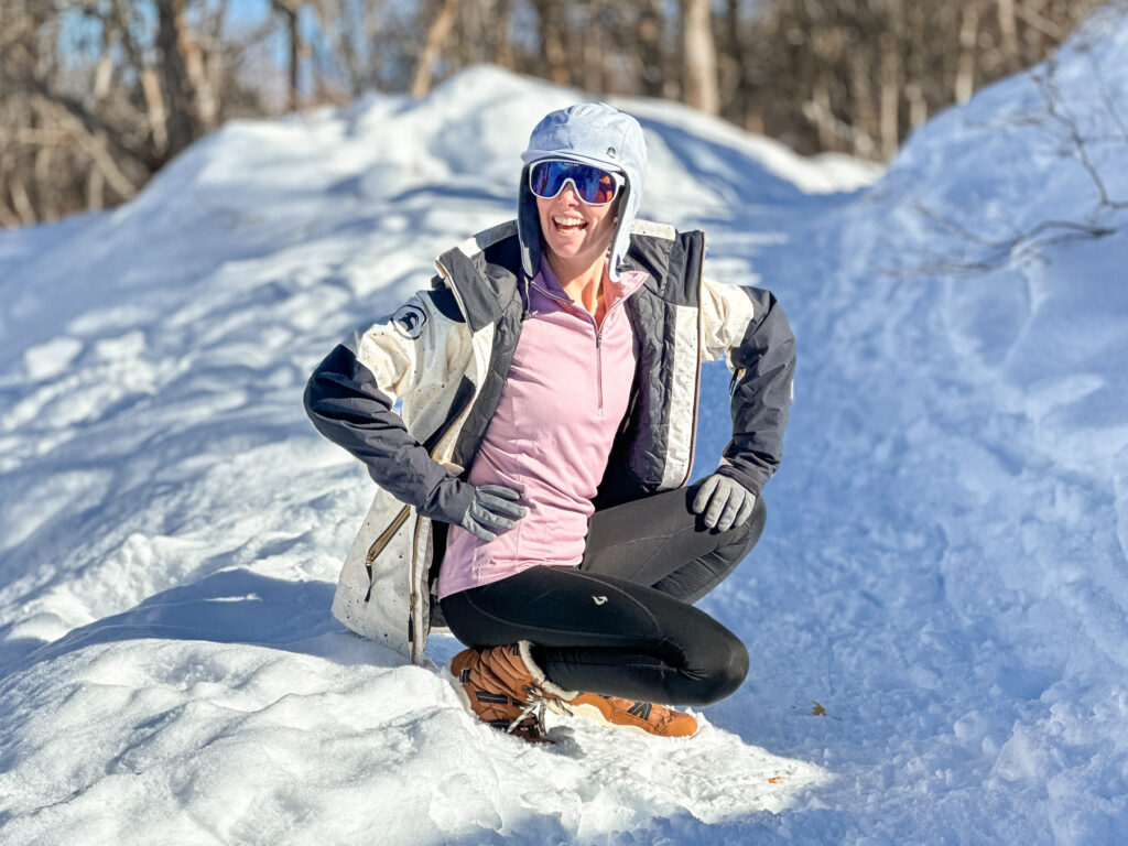 A woman squatting in the snow wearing Gnara Go Free Leggings.