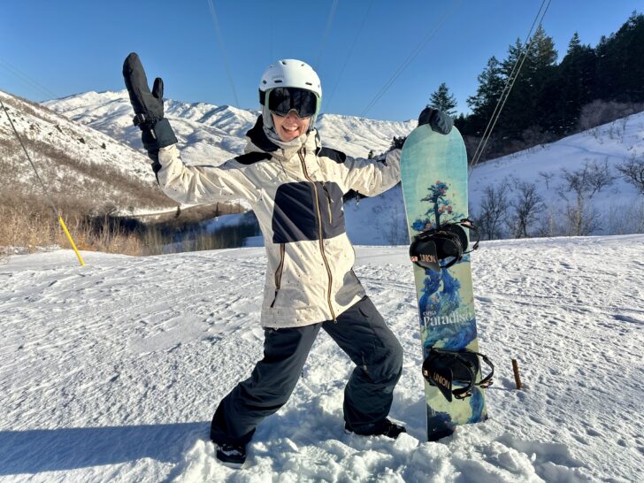 A woman poses with a snowboard in front of a mountain.