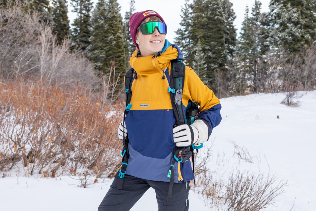 A woman wears a Paramo Velez Evolution Hybrid Smock in the snow while wearing a backpack.