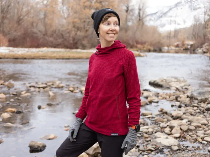 A woman smiles in front of a river. She wears a Squak Microgrid fleece hoodie.