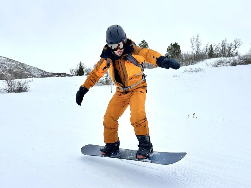 A man in a snowboard jacket and pants jumps with his snowboard on his boots.