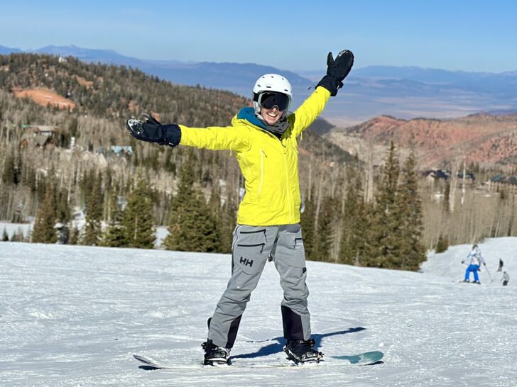 A woman in snowboard apparel smiles on a ski slope.