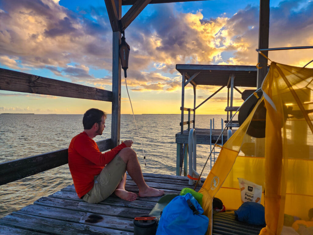 A man sits to enjoy sunset next to his tent on an on-water platform at Everglades National Park.