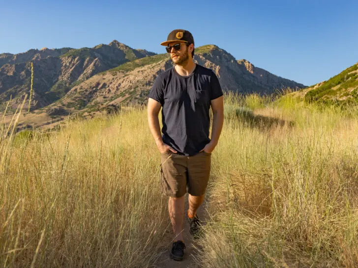 A man hiking in late afternoon sun wearing a t-shirt and shorts.
