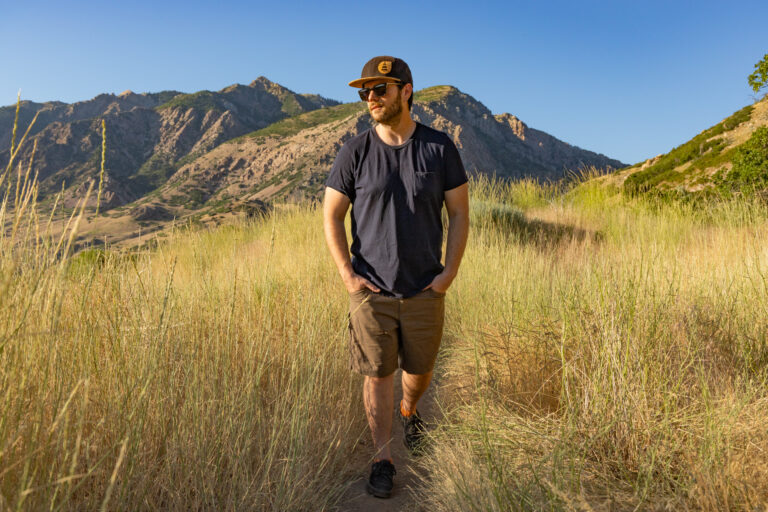 A man hiking in late afternoon sun wearing a t-shirt and shorts.