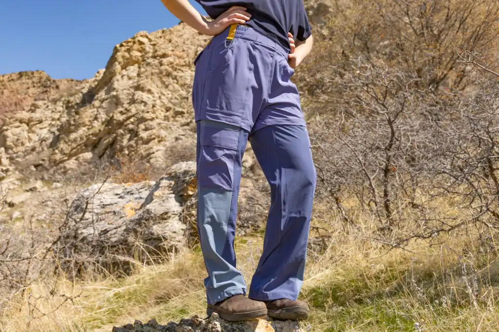 A woman's lower half wearing the Cotopaxi Losdos convertible hiking pants for women as she stands on a rock in front of cliffs.