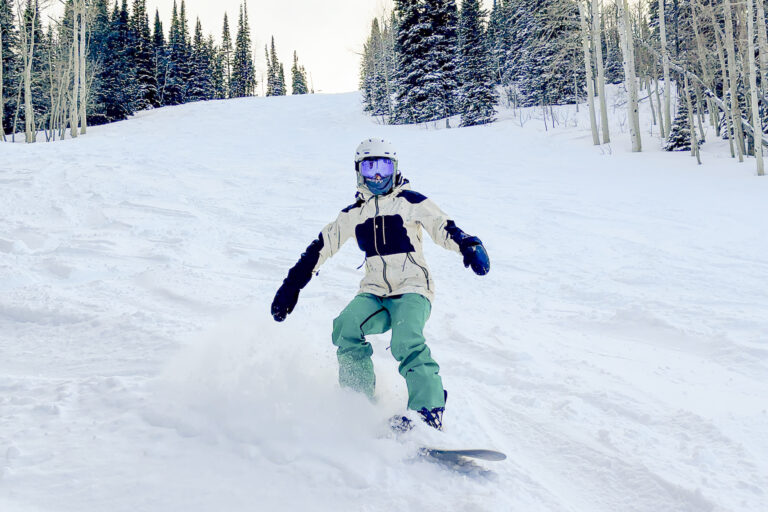 A woman snowboards in fresh powder wearing the Burton ski bibs with Gnara GoFly technology.