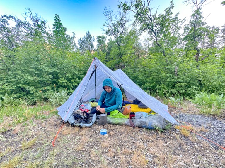 A man sits inside a Hyperlite Unbound 2 person ultralight backpacking tent with one vestibule open.