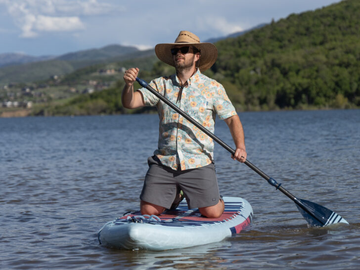 A man kneels on a paddle board in a large sun hat, Hawaiian shirt and Free Fly Apparel Reverb shorts.