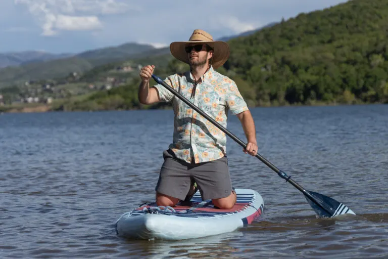 A man kneels on a paddle board in a large sun hat, Hawaiian shirt and Free Fly Apparel Reverb shorts.