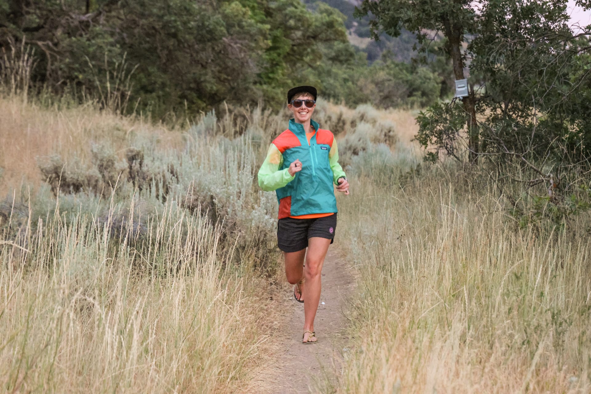 A woman trail runs in a windbreaker and barefoot running sandals.