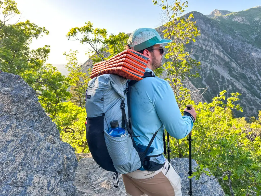 A man stands on a trail with the Gossamer Gear Skala 38 backpack on his back.