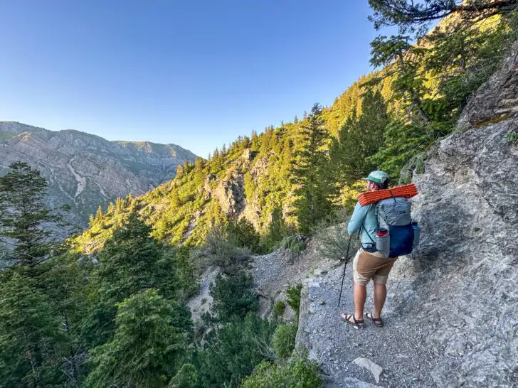 A man stands on a trail with the Gossamer Gear Skala 38 backpack on his back.