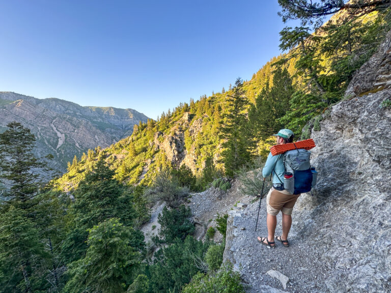 A man stands on a trail with the Gossamer Gear Skala 38 backpack on his back.