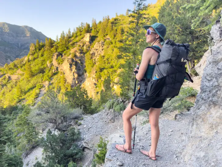 A woman stands on a hiking trail wearing the Symbiosis Gear Aspen backpack.