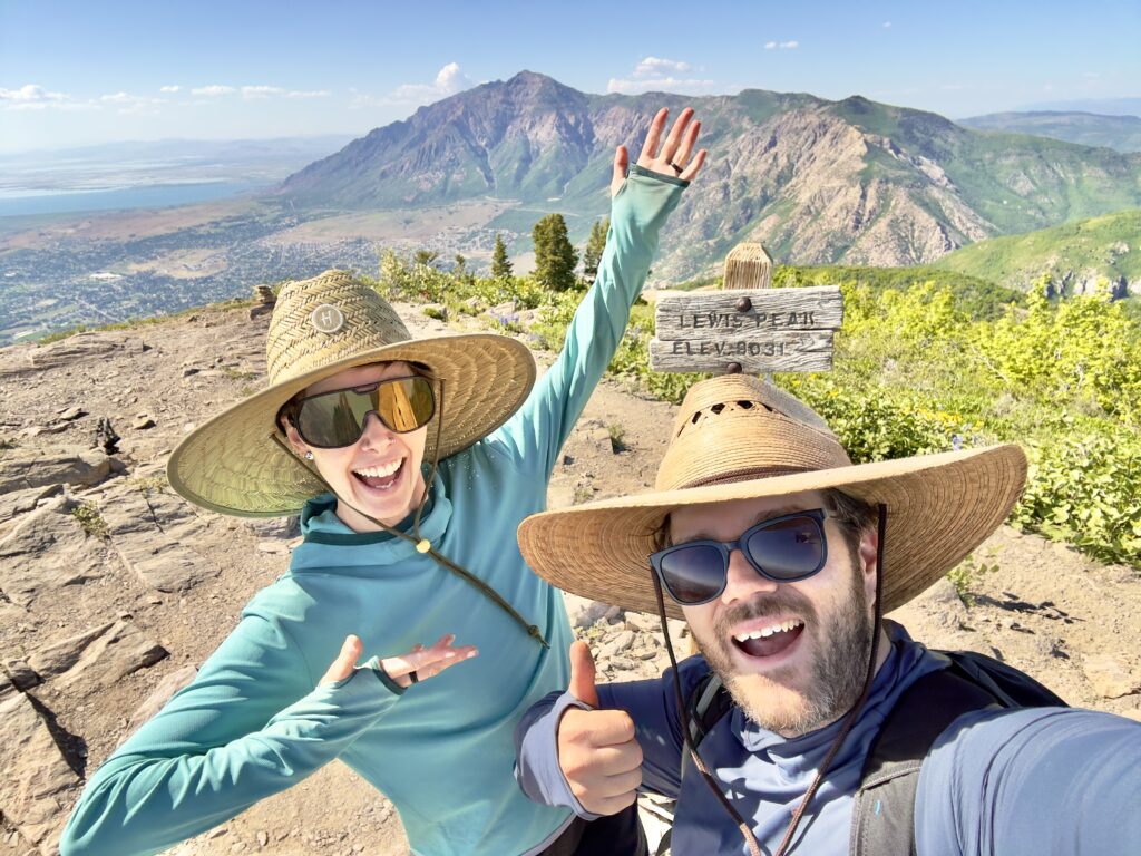 A man and woman in large sun hats smile excitedly from a peak.