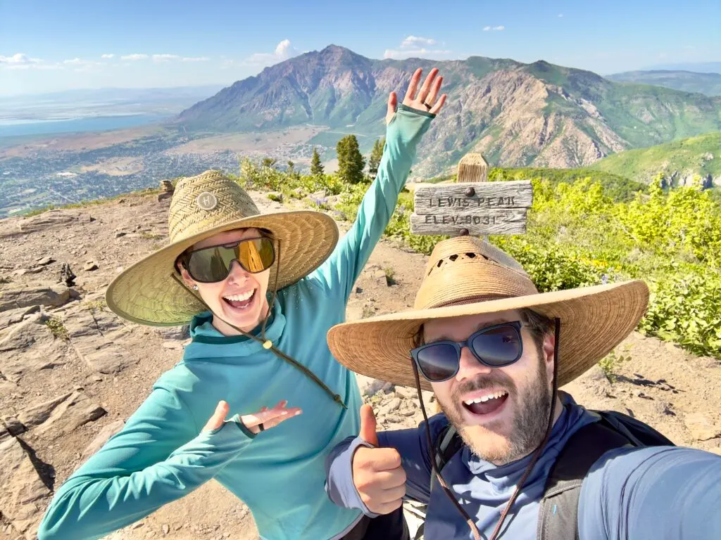 A man and woman in large sun hats smile excitedly from a peak.