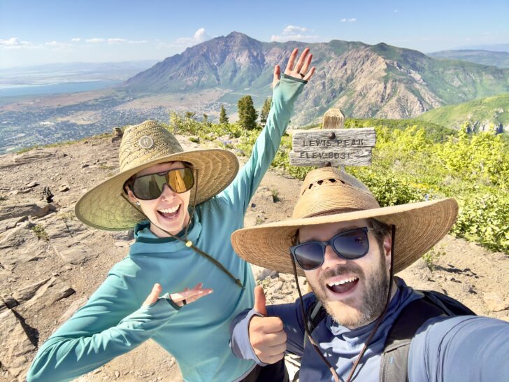 A man and woman in large sun hats smile excitedly from a peak.